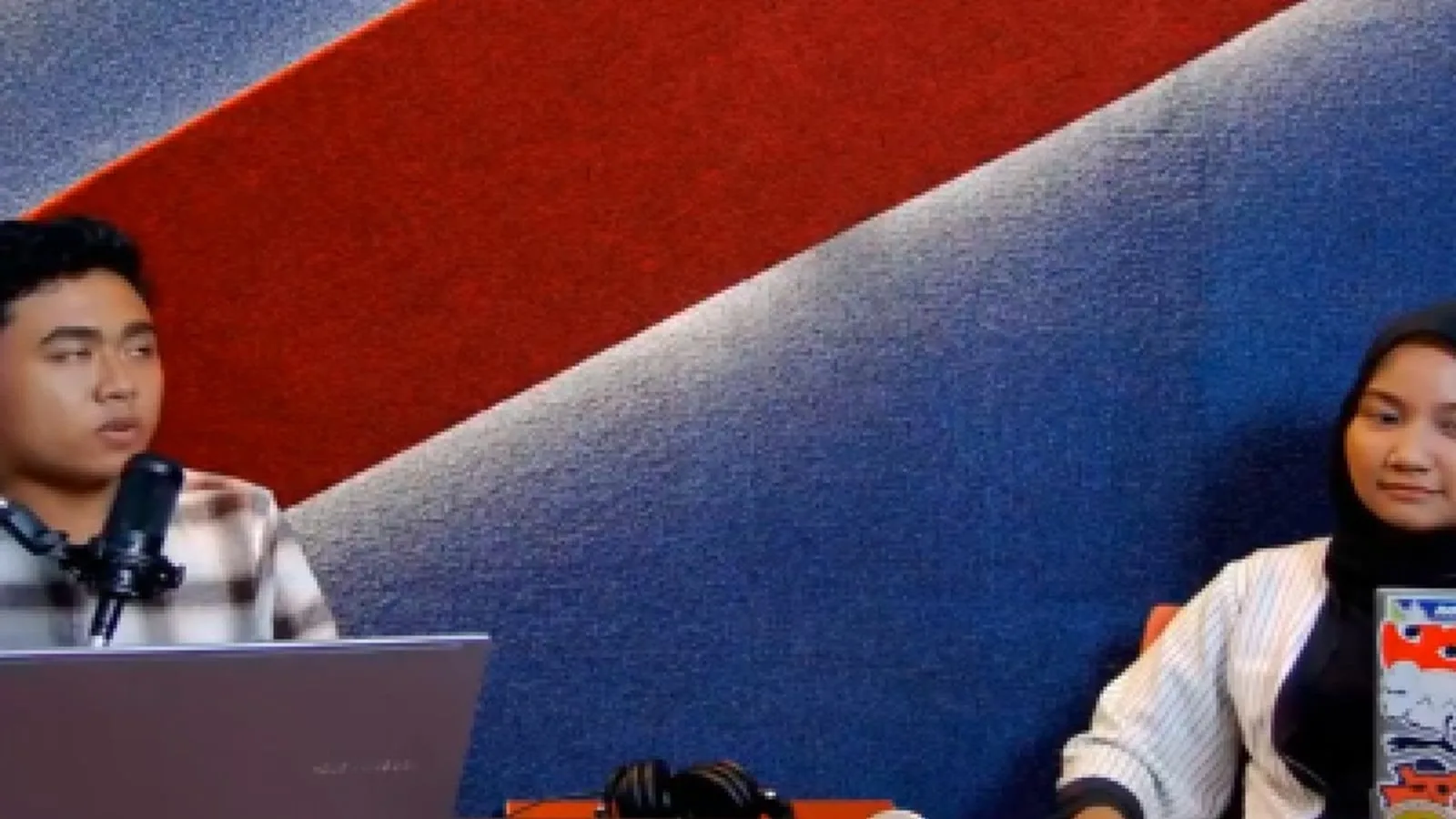 Dua pembawa acara di meja studio dengan mikrofon dan laptop, direkam untuk konten.